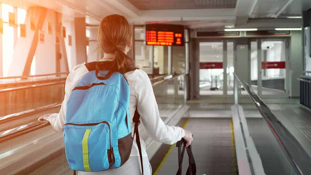 Woman on escalator with backpack and suitcase in airport terminal.