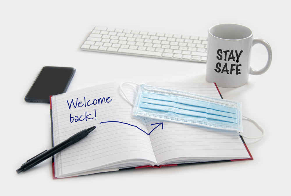 Welcome back to work concept. Medical protection mask waiting at the desk along with note pad, computer keyboard, phone, pencil and a coffee mug. Ready to work after the Coronavirus Covid-19 pandemic
