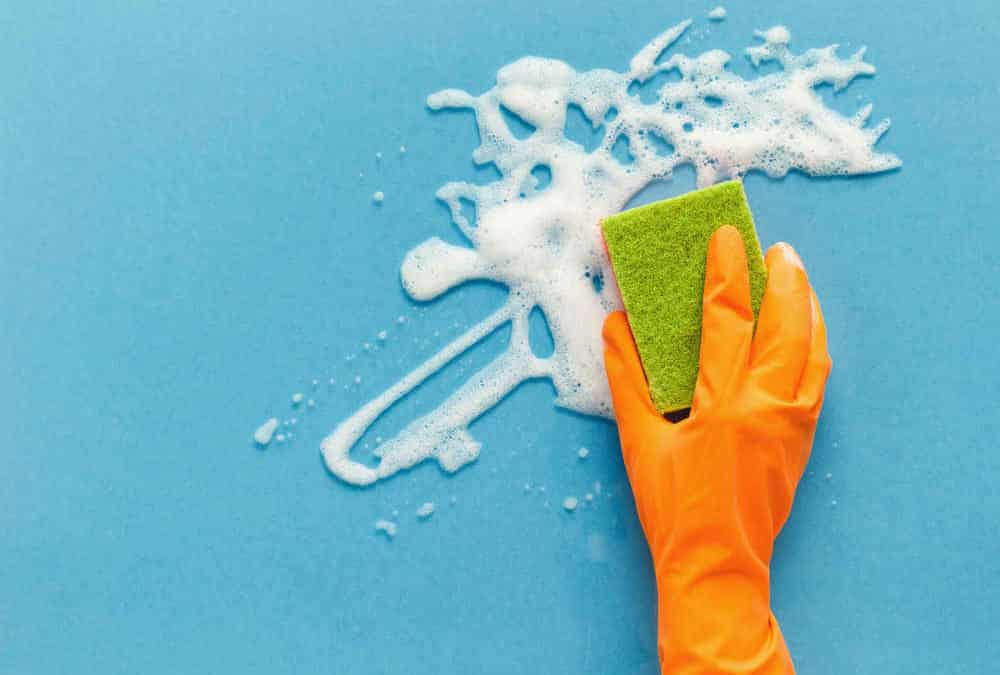 Hand in glove washing glass surface with sponge and cleaning foam